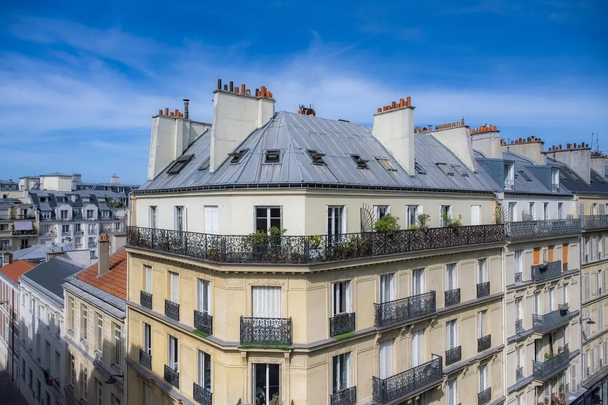 Immeuble d'angle parisien en pierre de taille, balcons en fer forgé et toiture en zinc avec souches de cheminée